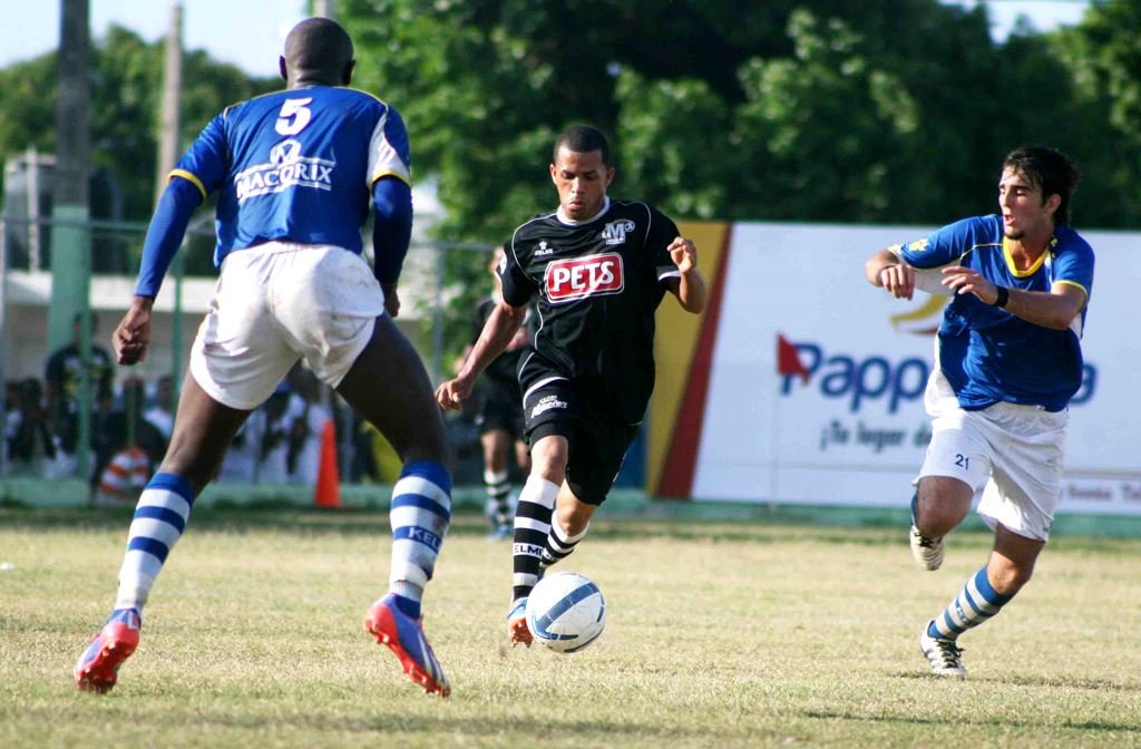 Ronald García maneja el balón ante dos defensas del Atlético de Puerto Plata